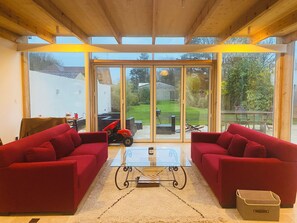 Ein geräumiges Wohnzimmer mit zwei roten Sofas, einem Glastisch und Blick durch große Schiebetüren in einen Garten.