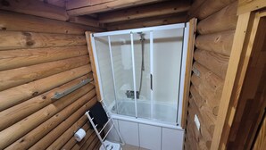 A wooden cabin with a glass-enclosed shower area, a towel rack, and a toilet.