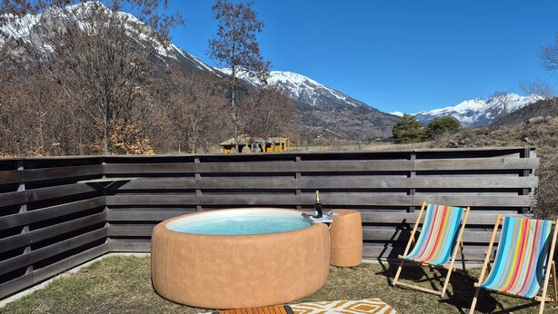 A hot tub, lounge chairs, and a patterned rug in a backyard with a mountain view.