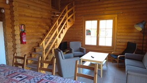 A log cabin interior with a wooden staircase, a television, a table, and two chairs.