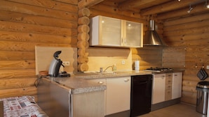 A kitchen with wooden walls, a granite countertop, a coffee maker, a sink, cabinets, and a trash can.