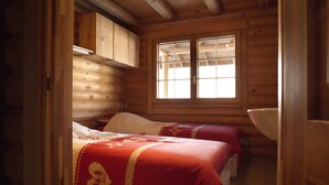 A cabin with two beds, wooden walls, a window, and a wooden cabinet.