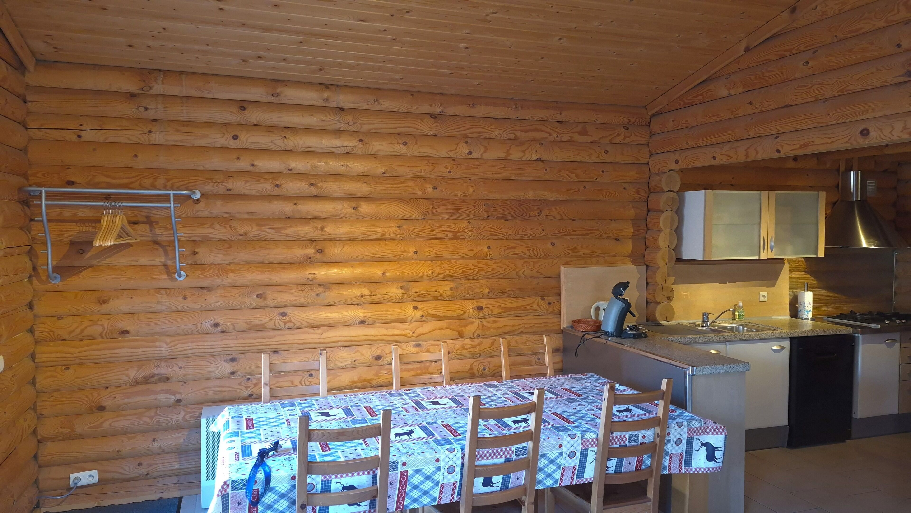 L’intérieur d’une cabane en rondins comprend une table à manger, des chaises, un coin cuisine et un étendoir suspendu.
