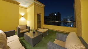 Een balkon met buitenmeubilair, een deur en een uitzicht op de stad 's nachts.