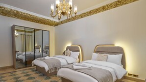 Een hotelkamer met twee bedden, een grote spiegel, een kroonluchter en een geruit vloerkleed.