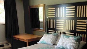 Un lit avec une couvre-lit à motifs, une table de chevet, un miroir et une tête de lit ornée d’un motif géométrique.