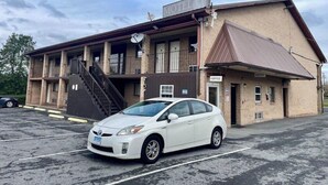 Un motel composé d’un bâtiment à deux étages, d’un escalier et d’un parking où se trouve une voiture blanche.