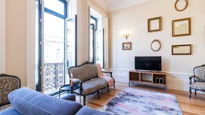 Een woonkamer met een bank, fauteuils, een televisie en een kamerkleed met een patroon.