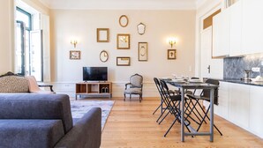 Een woonkamer met een bank, een televisie, een eethoek met een tafel en stoelen, en een keuken met kasten.