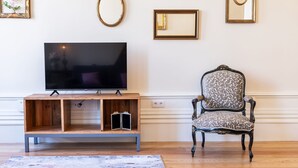 Een woonkamer met een televisie op een houten standaard, een fauteuil met een patroon en drie wandspiegels.