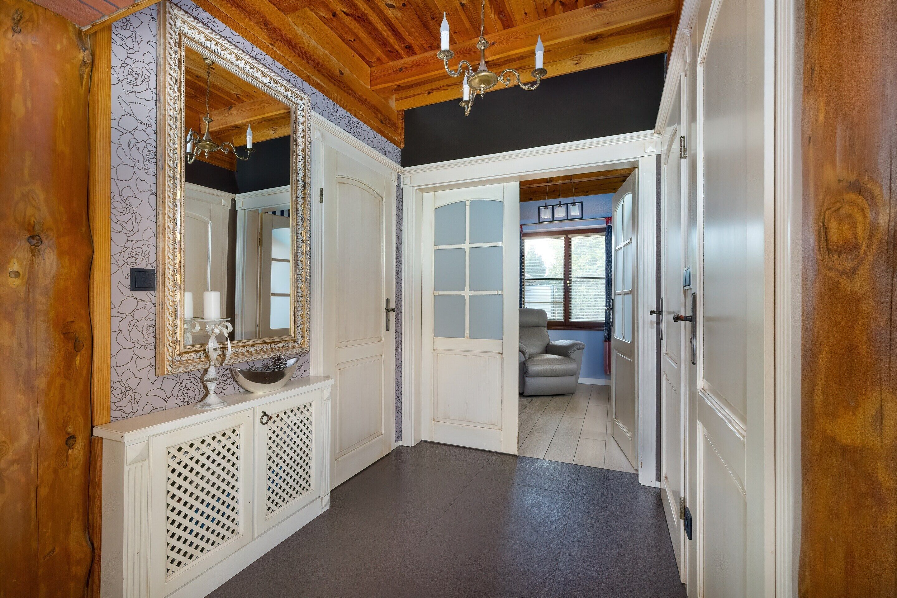 A hallway with a wooden ceiling, a large mirror, and a chandelier.