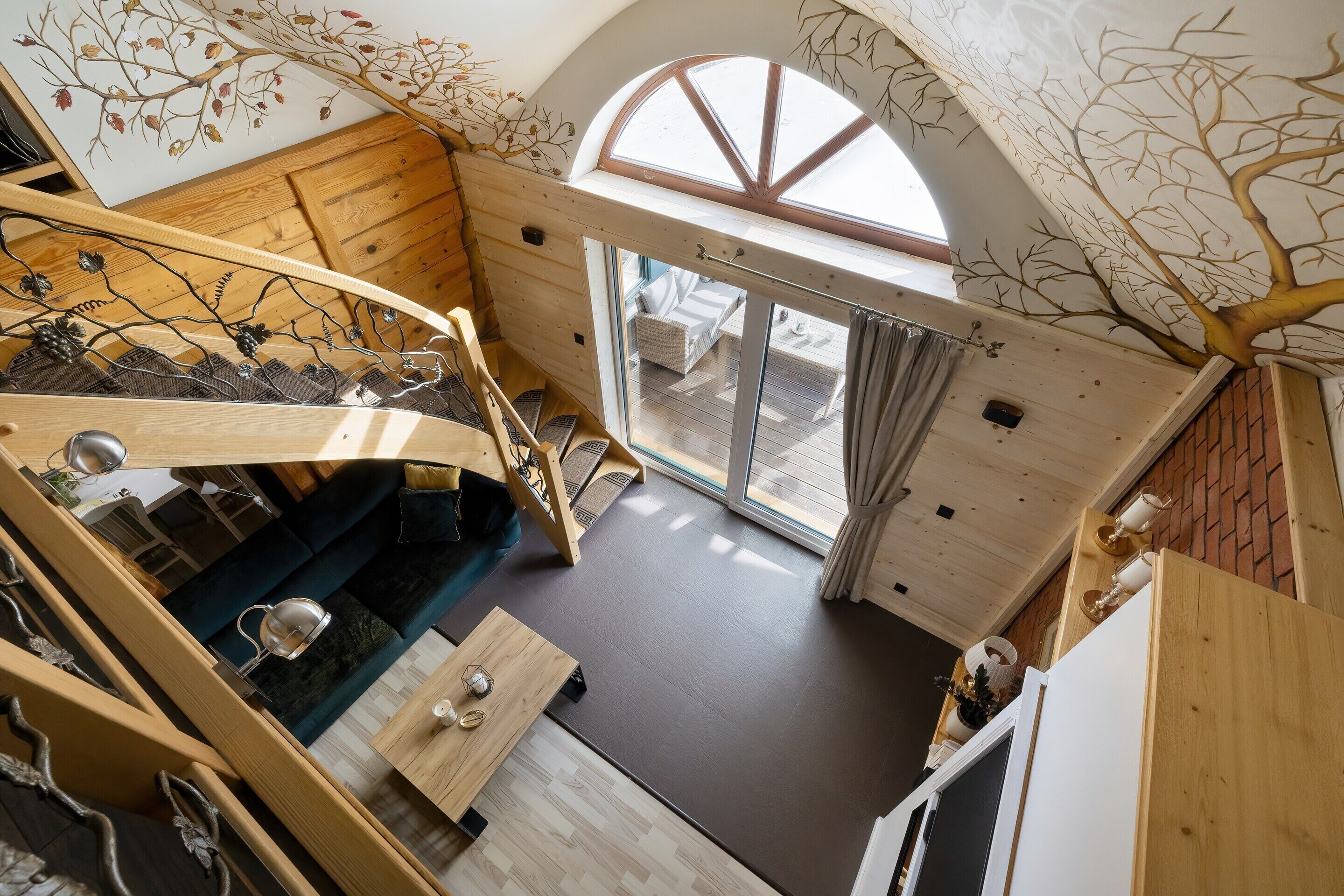 Un intérieur en bois avec un escalier, un canapé, une table et une vue à travers une porte vitrée.