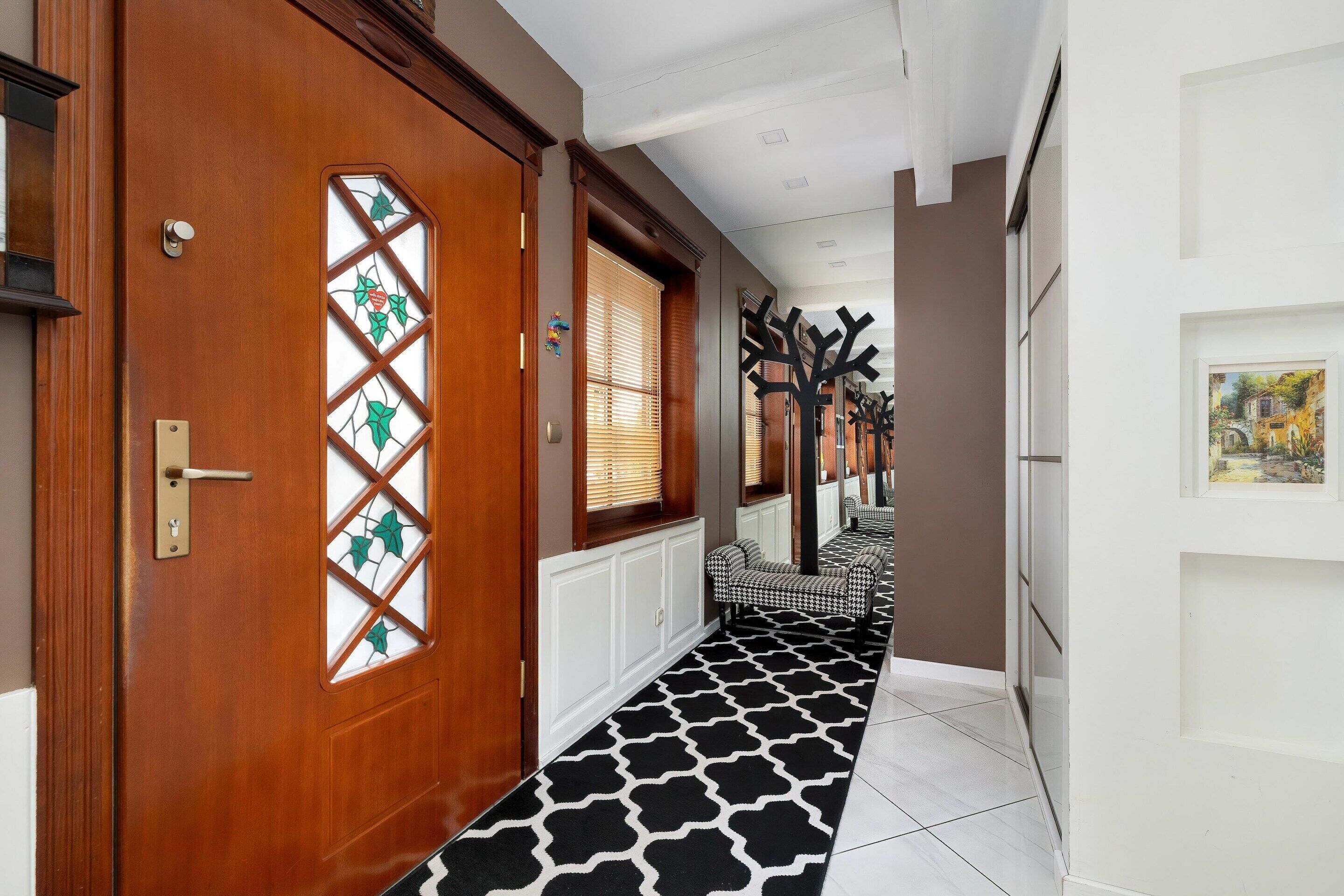 Um corredor com porta de madeira, tapete estampado e um banco.