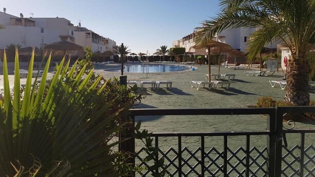 A pool area with lounge chairs, palm trees, and buildings in the background. - Apartment in Natura World With Pool (Vera)