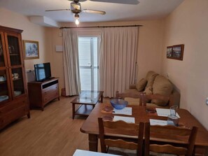 A dining area with a table, chairs, a television, and a cabinet. - Apartment in Natura World With Pool (Vera)