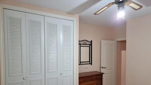 A room with a white wardrobe, a wooden dresser, a mirror, and a ceiling fan. - Apartment in Natura World With Pool (Vera)