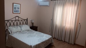 A bedroom with a bed, a nightstand, a lamp, an air conditioner, and a window with curtains. - Apartment in Natura World With Pool (Vera)