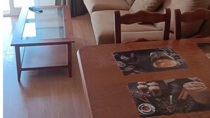 A living room with a glass-top coffee table, a beige sofa, and a wooden dining table with placemats. - Apartment in Natura World With Pool (Vera)