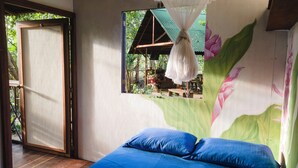 Ein Zimmer mit einem Bett, einem Fenster mit Blick auf eine Holzkonstruktion und einer Wand mit floralem Wandbild.