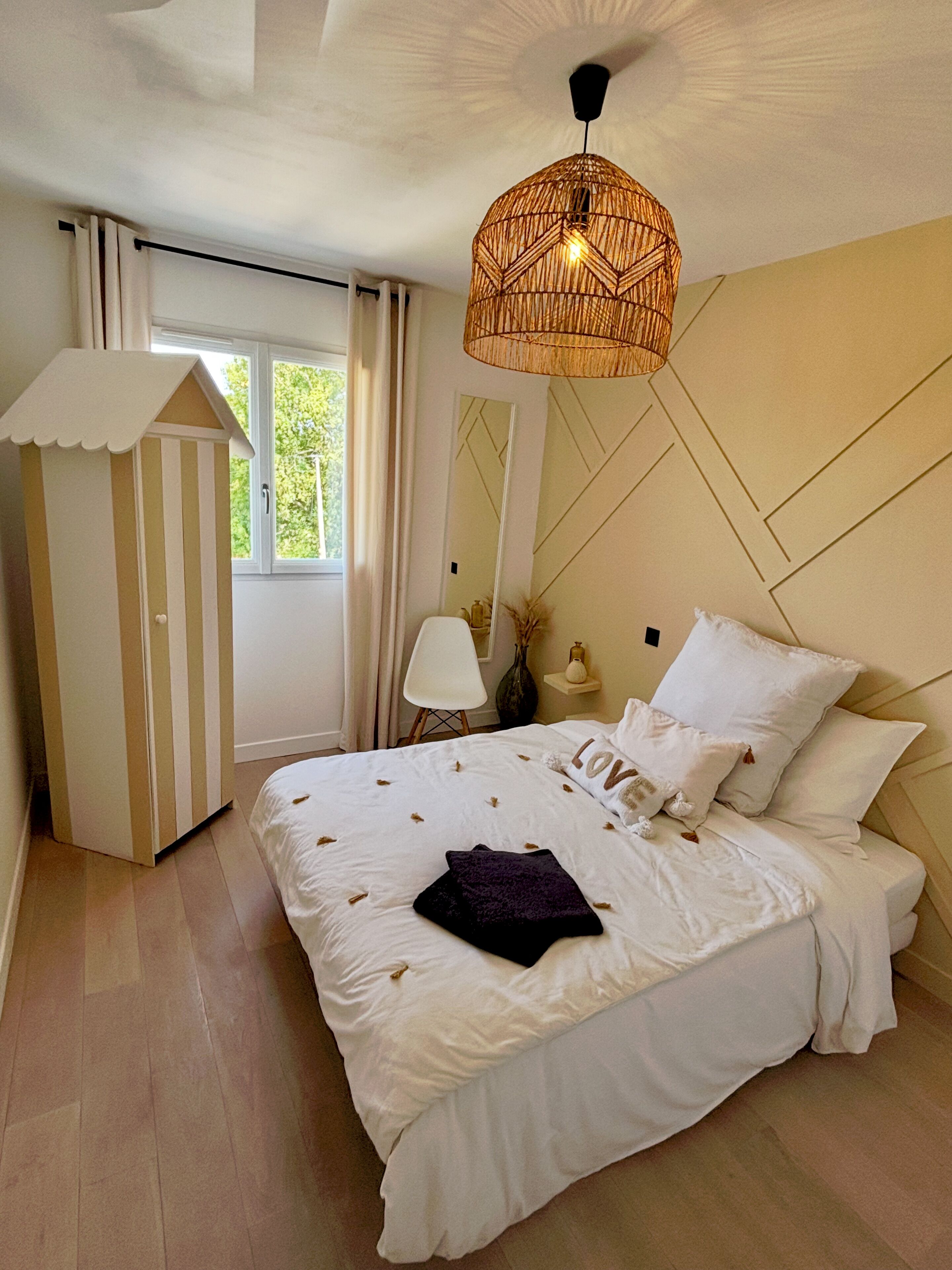 Un dormitorio con cama, lámpara colgante, ventana y un mueble a rayas.