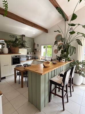 A kitchen with a central island, wooden chairs, and potted plants. - Villa 5 minutes from the sea! Near Royan (Semussac)