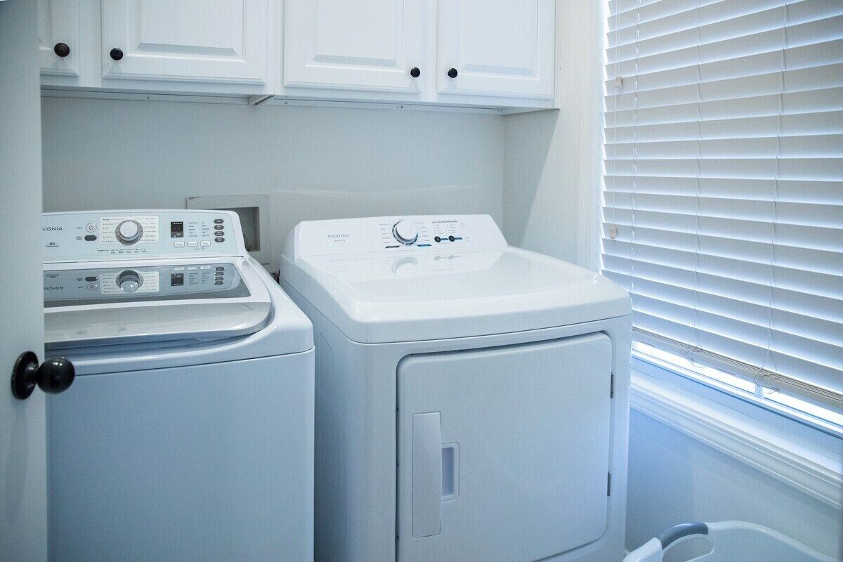 Une buanderie équipée de deux machines à laver, d’un sèche-linge et d’un meuble de rangement placé au-dessus des machines.