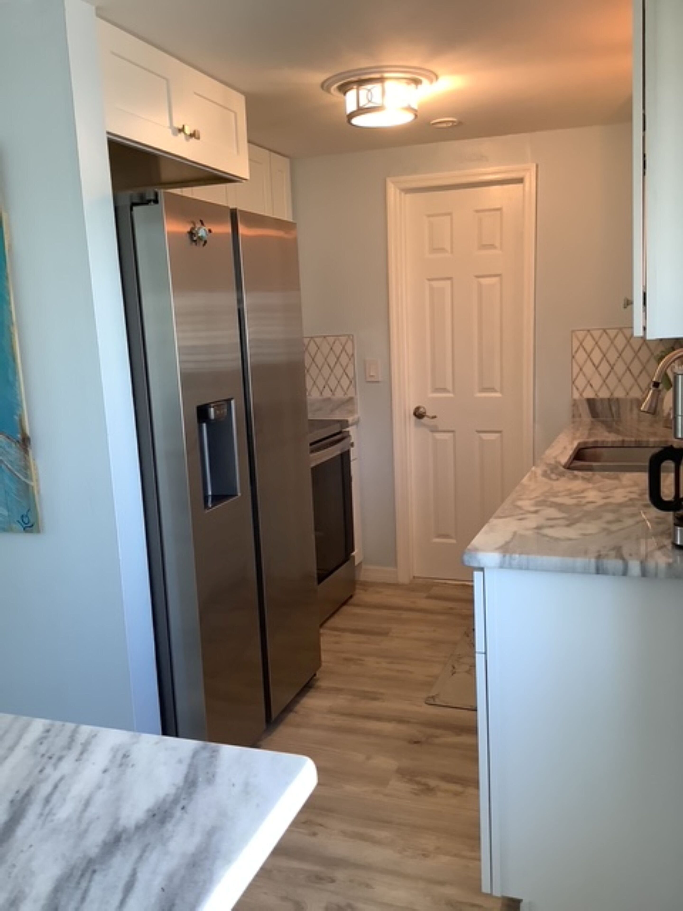 A kitchen with a stainless steel refrigerator, a wooden floor, and a white door.