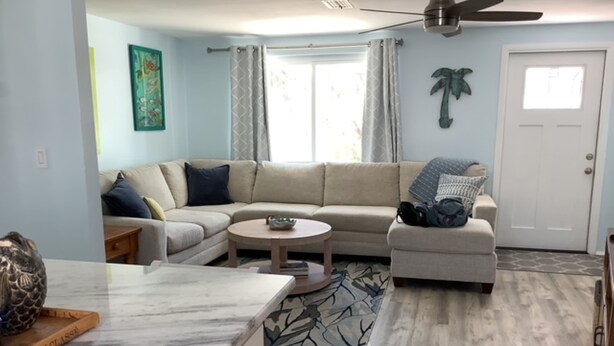 A living room with a sectional sofa, a round coffee table, and a kitchen area with a marble countertop.