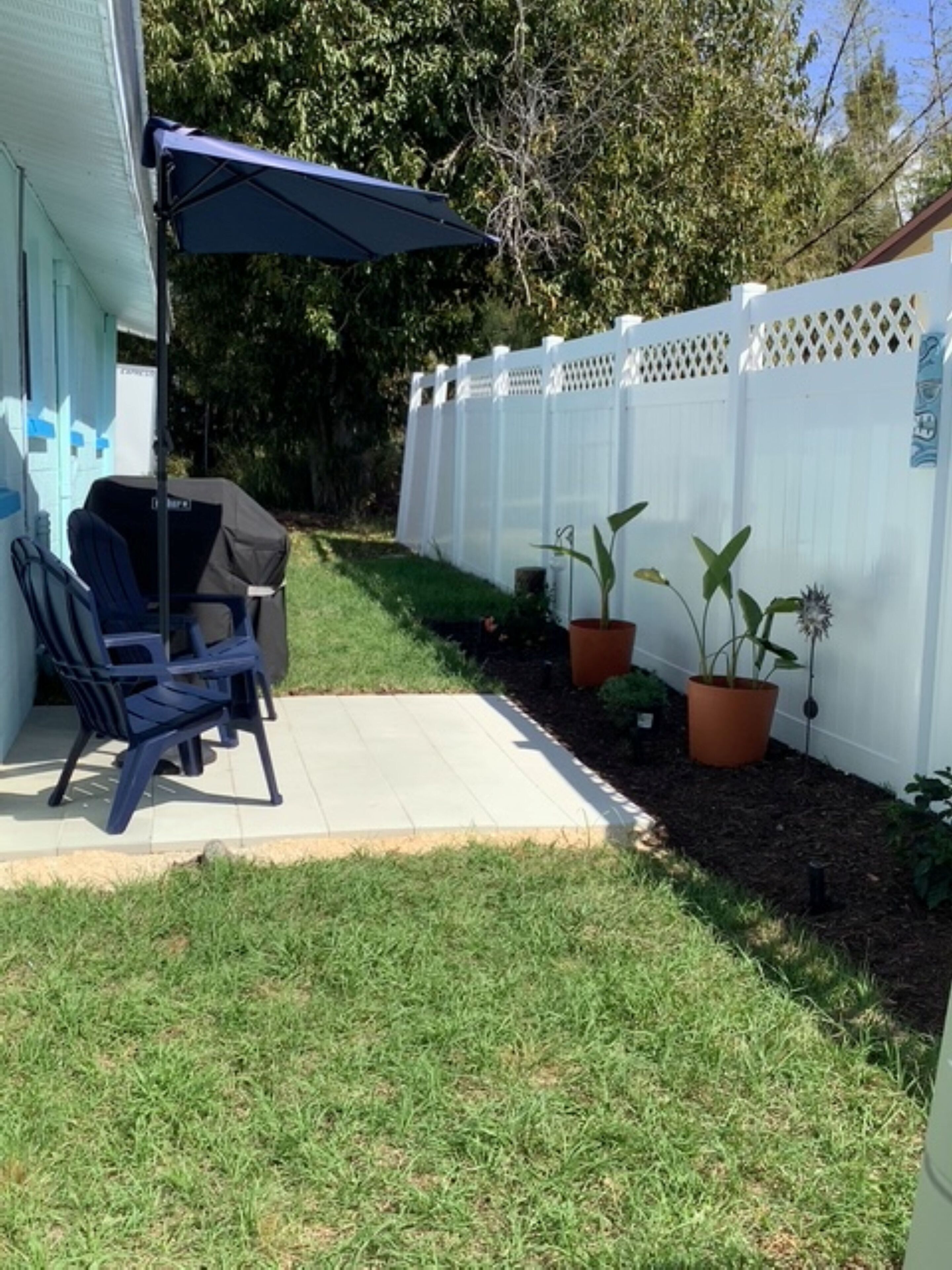 Un patio con zona de estar techada, una parrilla y plantas en macetas.