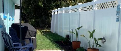 Un patio con zona de estar techada, una parrilla y plantas en macetas.
