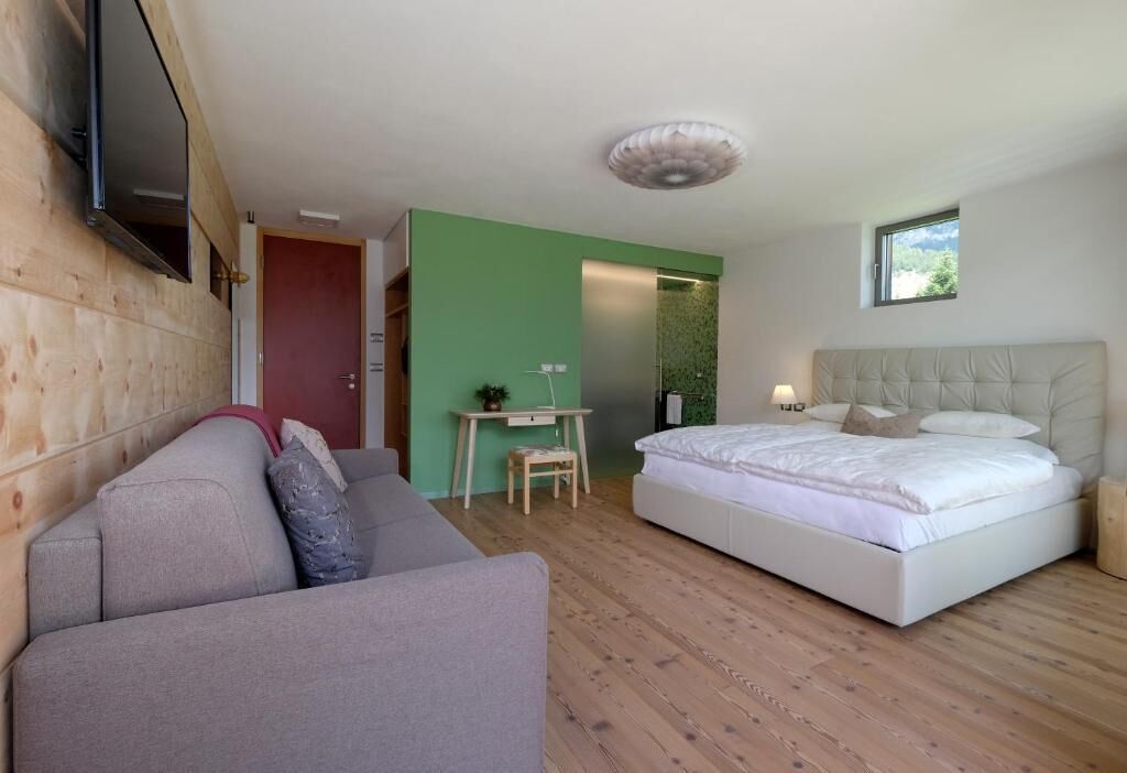 A bedroom with a bed, a desk, a chair, and a television mounted on the wall.