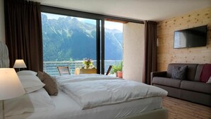 Habitación de hotel con cama, sofá, televisión y vistas a montañas.