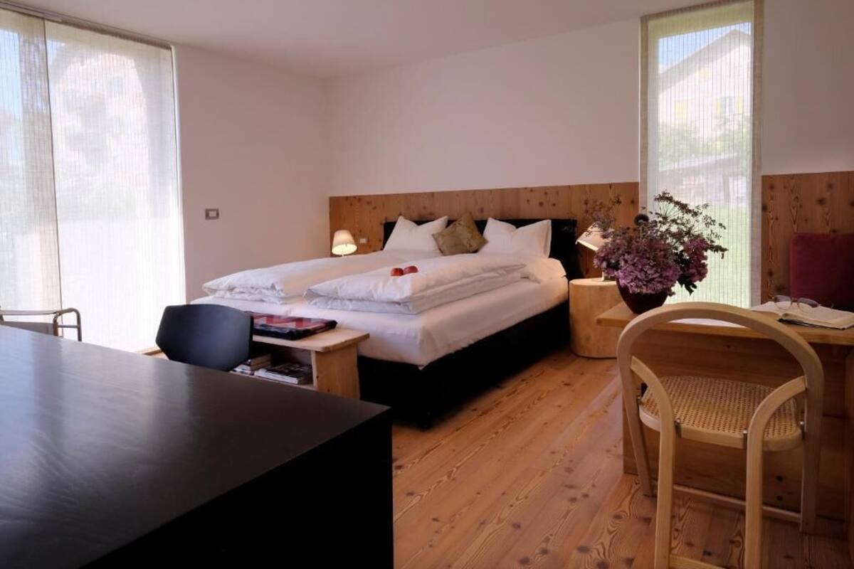 A bedroom with a bed, bedside table, lamp, chair, and a desk.