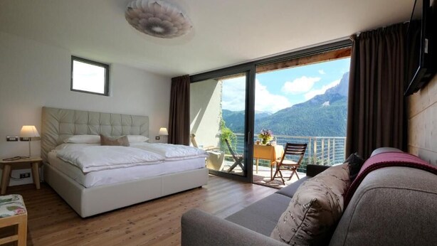 Un dormitorio con cama, sofá, mesa con sillas y balcón con vista a la montaña.