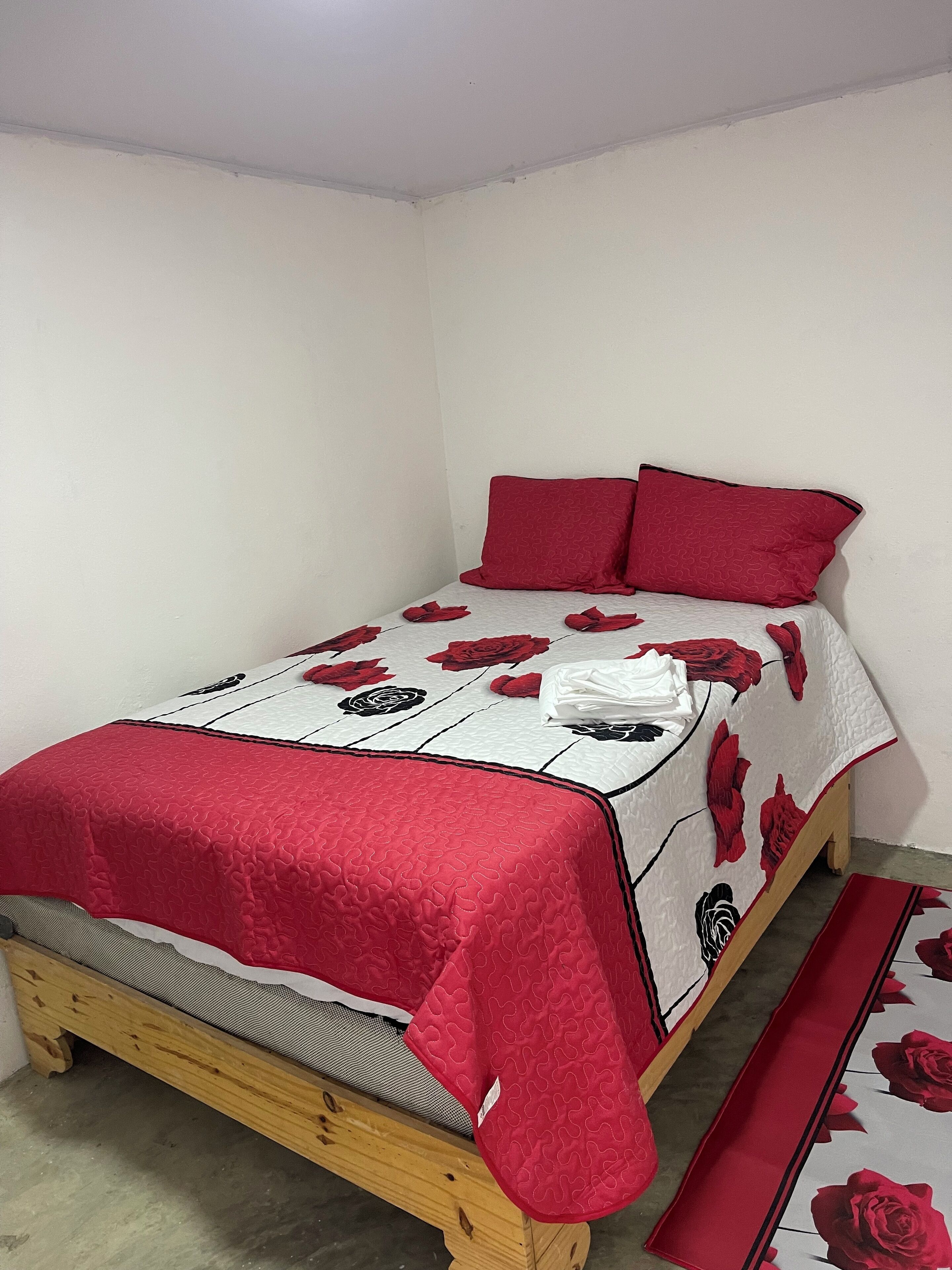 A single bed with a red and white floral bedspread, two red pillows, and a matching red runner.
