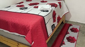 Una cama con una colcha blanca y roja con estampado floral, dos almohadas rojas y un corredor rojo.