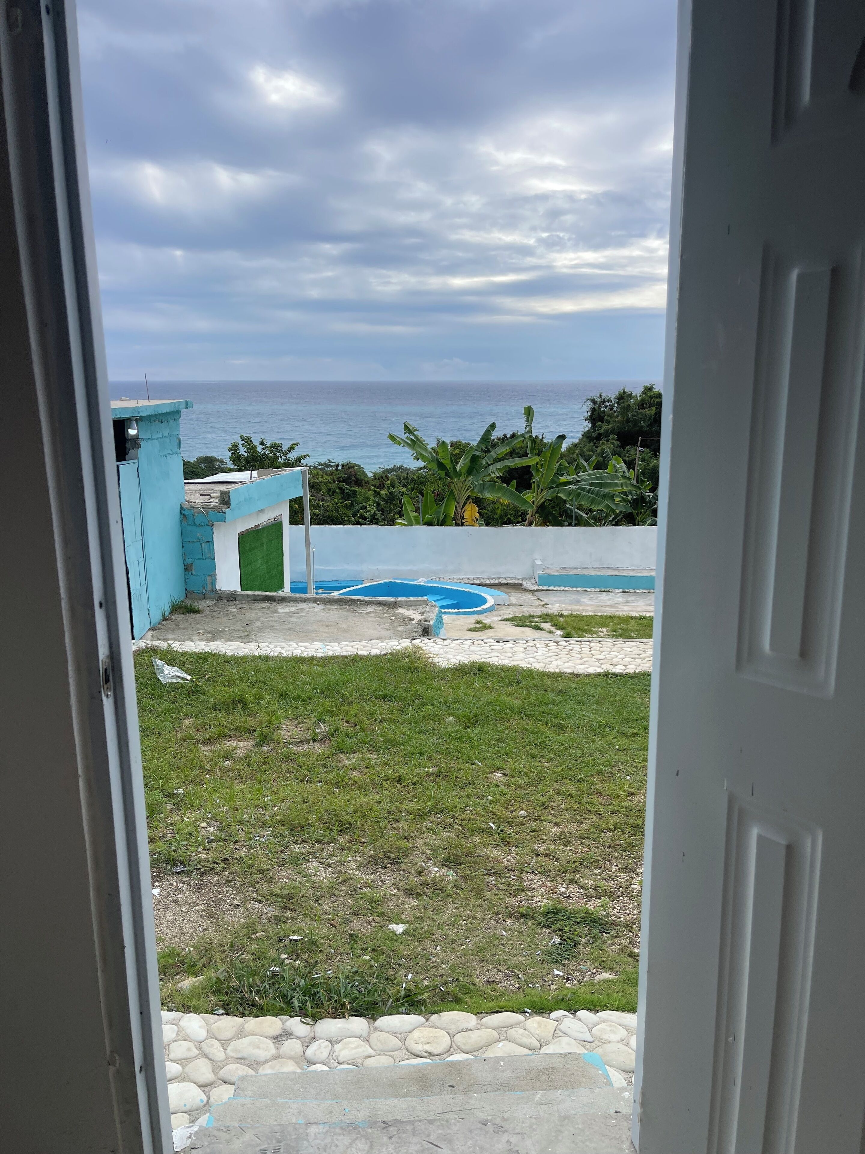 Une vue depuis une pièce, à travers une porte ouverte, qui donne sur une piscine, une pelouse et une étendue d'eau en arrière-plan.