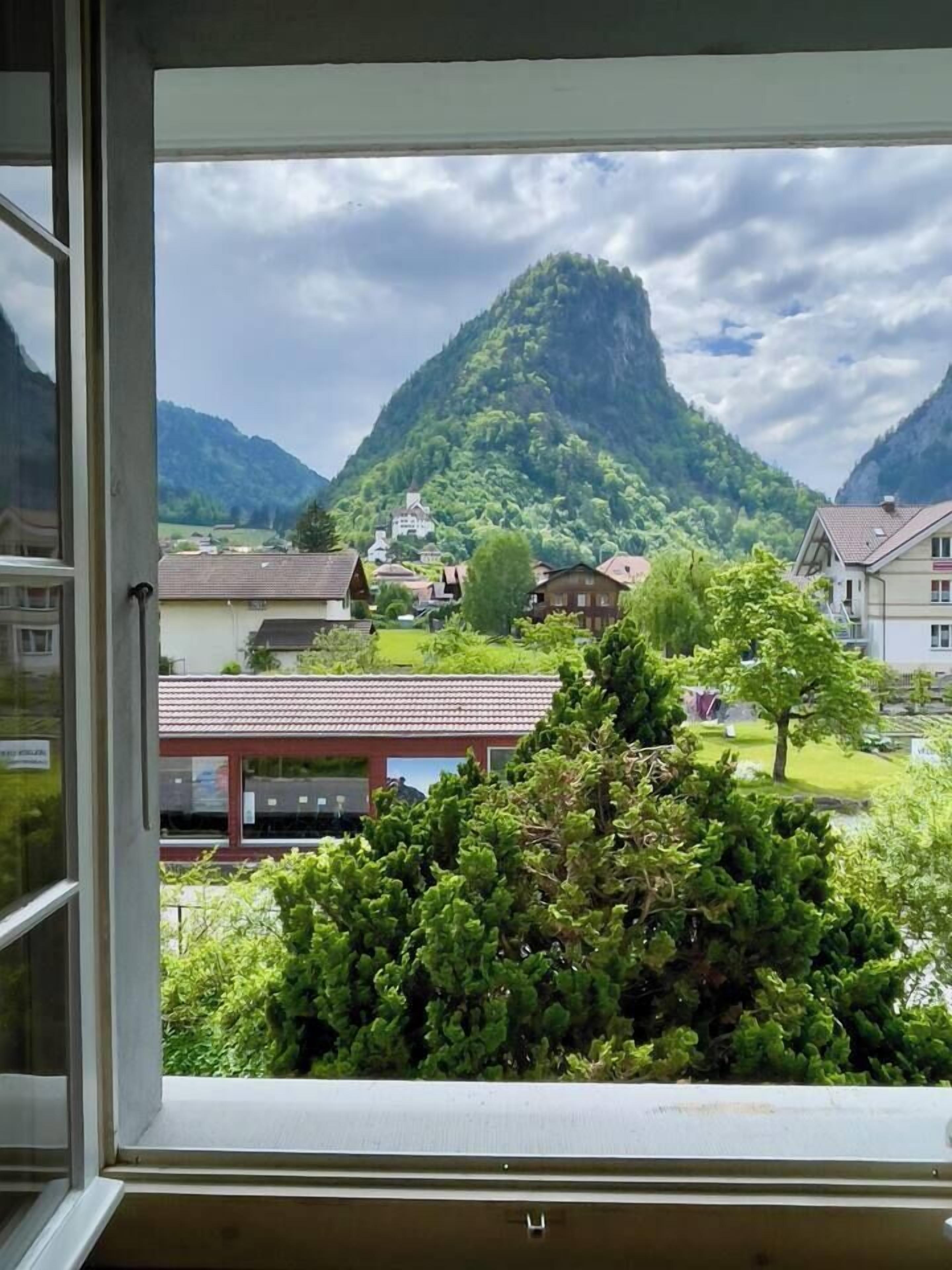 Vista desde una ventana que muestra un paisaje montañoso con edificios y vegetación.