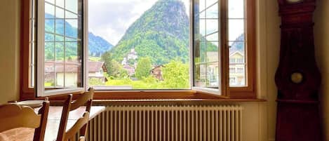 A room with a large window, wooden chairs, a radiator, and a clock.