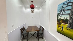 A narrow hallway with a wooden dining table and chairs, a red pendant light, a wall clock, and a large abstract painting. - Bright & Modern Apartment in the Heart of Almadies (dakar)