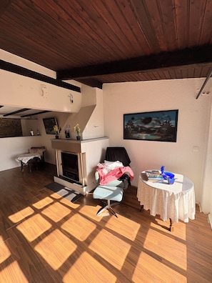 Una habitación con chimenea, una mesa con un florero, una silla y un cuadro en la pared.