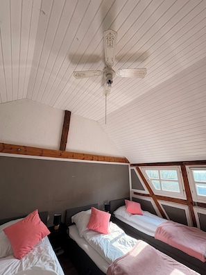 Una habitación con literas, ventilador de techo, vigas de madera y ventana con vistas.