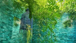 Un jardín interior con pared de ladrillo, plantas colgantes y una jaula de pájaros.