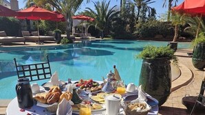Desayuno junto a una piscina, con mesa, sillas y sombrillas.