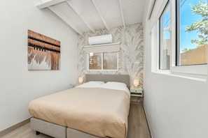 Un dormitorio con cama, lámparas de noche, ventana y equipo de aire acondicionado.