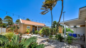 A house with a patio, outdoor seating, and a garden with various plants. - Walts Aruba (Noord)