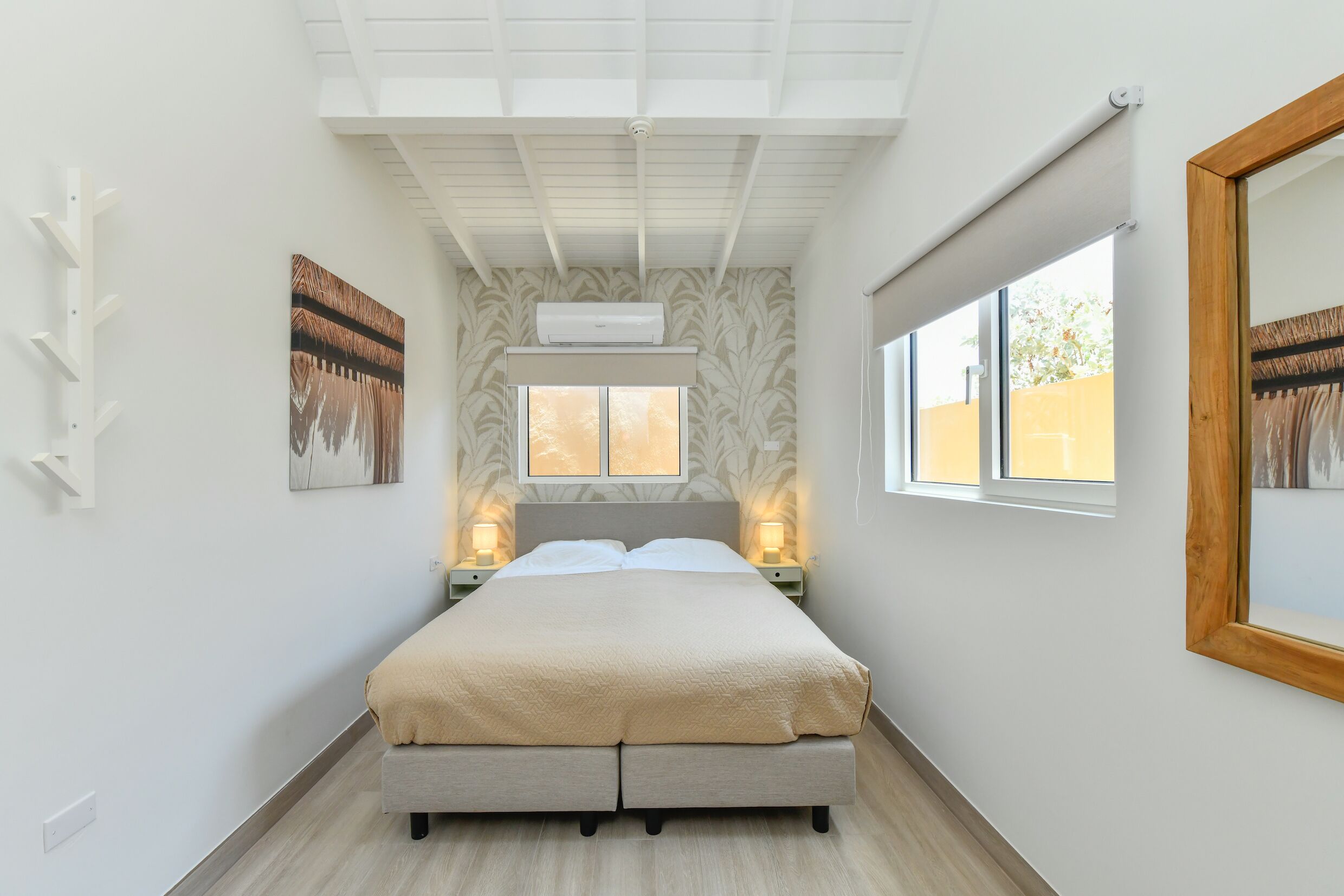 A bedroom with a bed, bedside lamps, a window, and a wall-mounted air conditioner.