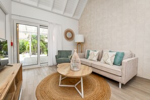 Una sala de estar moderna con un sofá, una mesa de centro de madera, una lámpara y vistas a través de un ventanal.