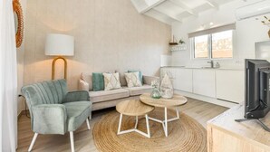 A modern living room with a sofa, a round coffee table, a lamp, and a television. - Walts Aruba (Noord)