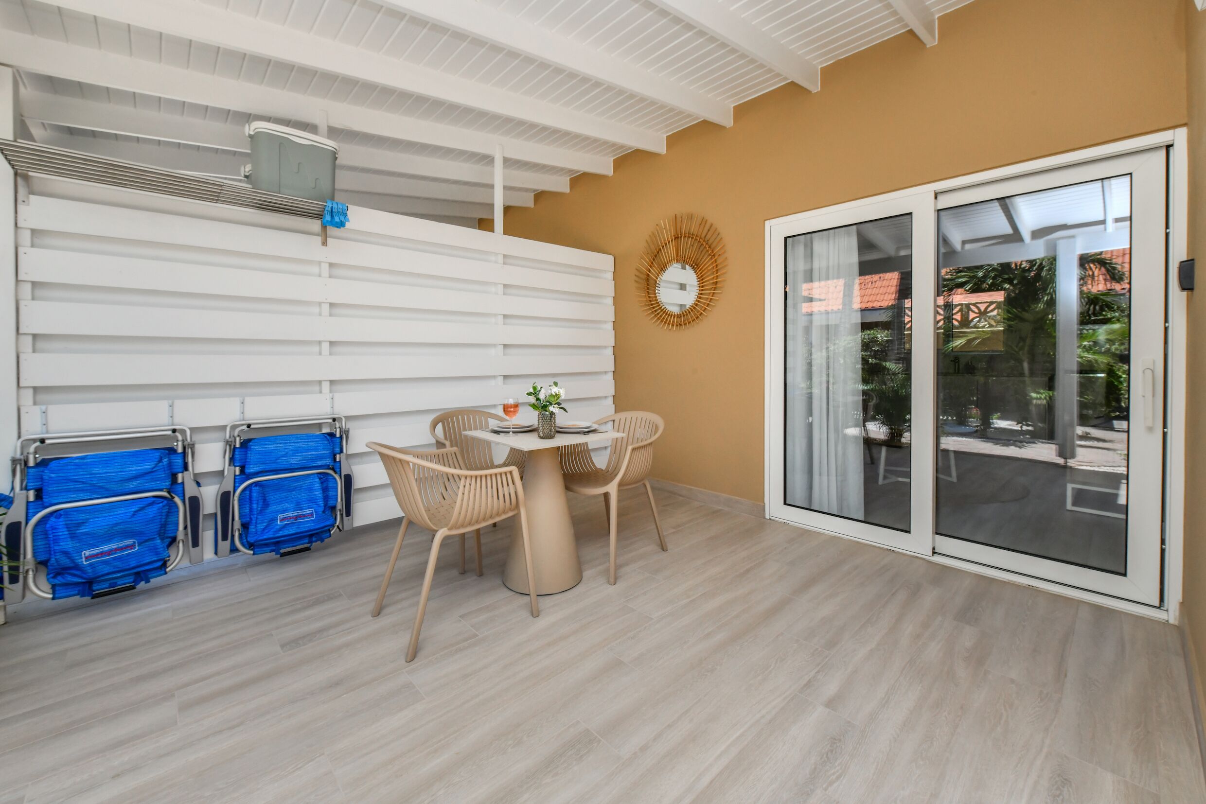 A room with a round table, two chairs, a wall-mounted air conditioning unit, and a sliding glass door leading to an outdoor area.